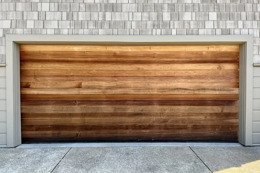 A garage door with horizontal wood grain planks on a shingled home